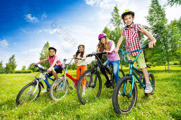 戴着五颜六色自行车头盔的快乐的孩子们抱着自行车