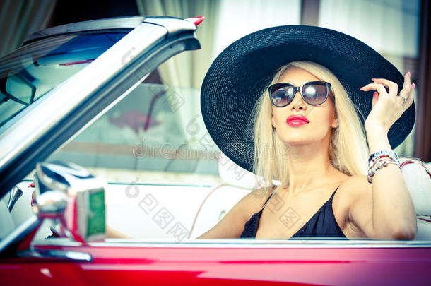 户外夏季画像时尚金发复古女人驾驶敞篷红色复古车。时尚迷人的金发女孩