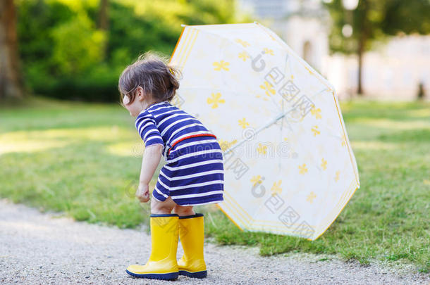 夏日公园里可爱的小男孩穿着黄色雨靴和雨伞