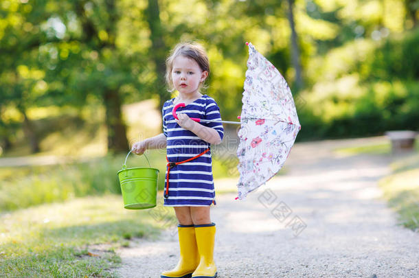 夏日公园里可爱的小男孩穿着黄色雨靴和雨伞