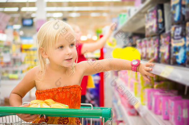 购物车里可爱的女孩看着超市货架上的商品