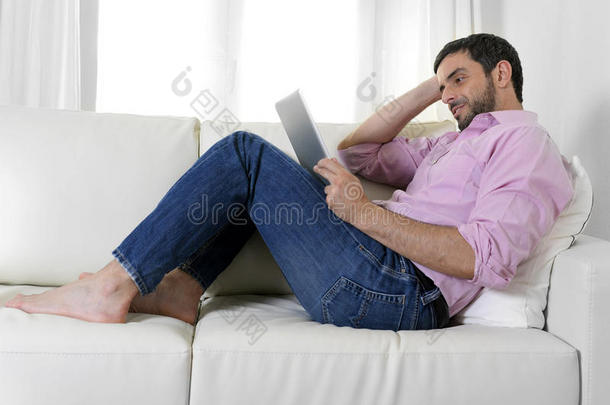 坐在沙发上用数字键盘或平板电脑的年轻快乐迷人的男人