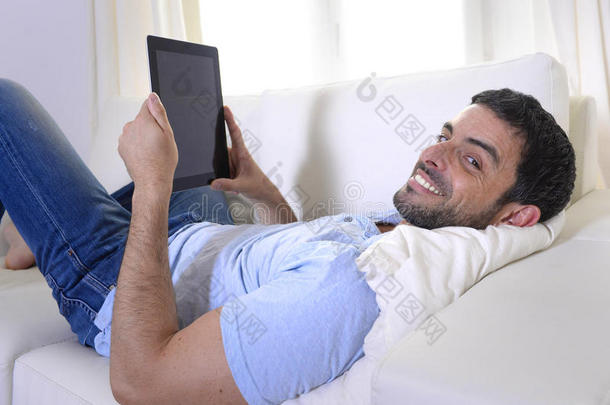 坐在沙发上用数字键盘或平板电脑的年轻快乐迷人的男人