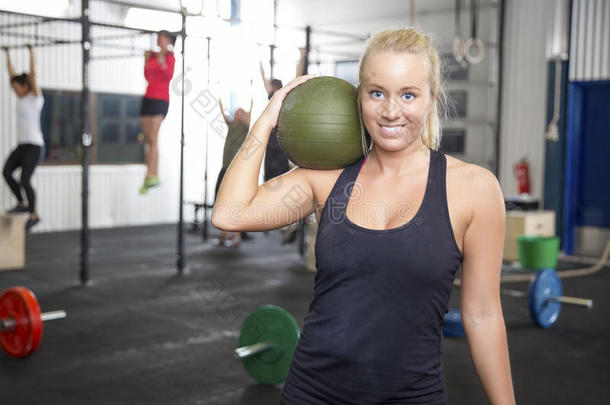 一个微笑着的金发女人在健身馆里拿着一个大满贯的球