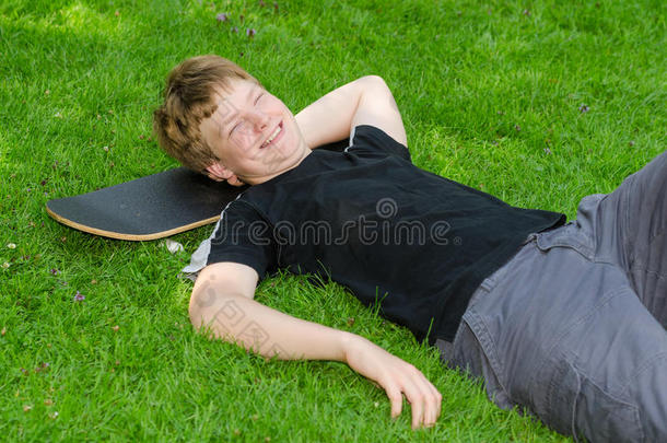 笑男在公园草地上的滑板上放松