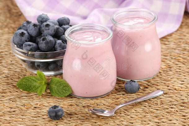 玻璃罐里放着蓝莓酸奶，垫子上的玻璃碗里放着蓝莓