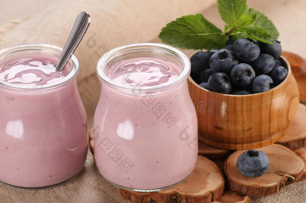 玻璃罐里放着蓝莓酸奶，玻璃碗里放着蓝莓，背景布上放着蓝莓