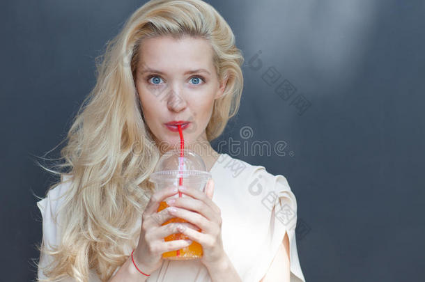 一个美丽的金发碧眼的女孩在炎热的夏天靠着墙边的吸管喝饮料