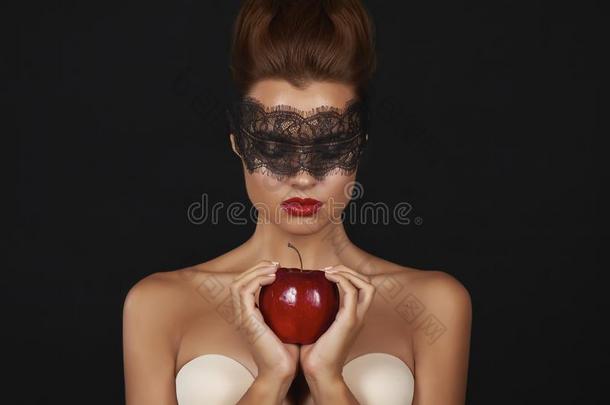 年轻漂亮的女人，眼睛上戴着深色蕾丝，光着肩膀和脖子，捧着<strong>大大</strong>的红苹果，尽情地品尝着美味