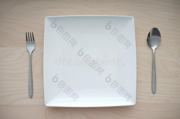 用叉子和勺子放在木桌上的空方形盘子