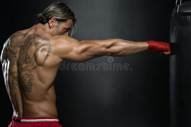赤膊肌肉拳击手与打孔袋在健身房