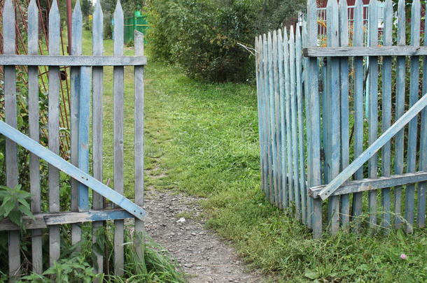 在一个有着土地、草地和树木的村庄里，一扇蓝色的破烂的大门通向达卡花园