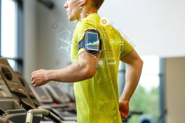 带着智能手机的男人在健身房的跑步机上锻炼