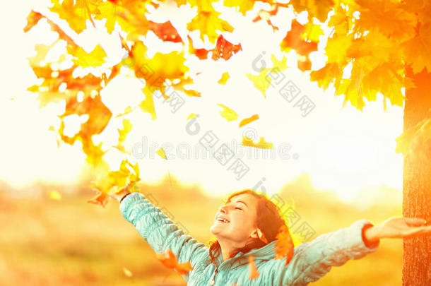 秋叶飘落的秋树下，高举双臂的年轻女子