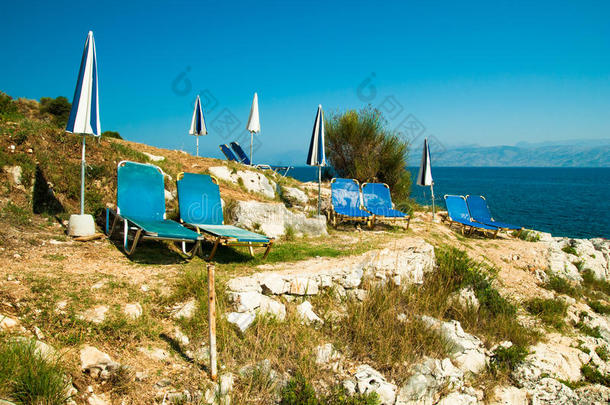 希腊科孚岛岩石海滩上的日光浴床和雨伞（阳伞）。