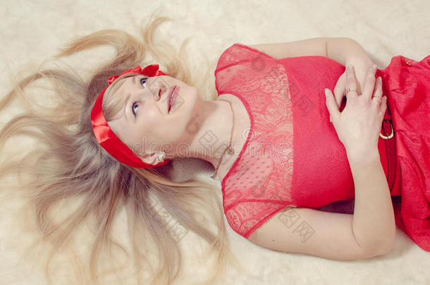 <strong>浪漫甜美</strong>迷人的金发女孩，穿着红色连衣裙，头上系着丝带，放松地躺着，开心地笑着抬头看