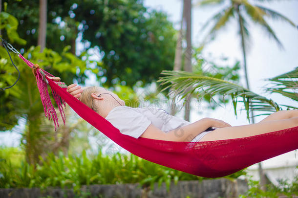 一位漂亮的年轻女士在热带海滩上的橡树下的小山丘里听音乐