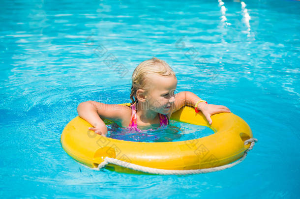 可爱的女孩在海滩游泳池的黄色救生圈上游泳