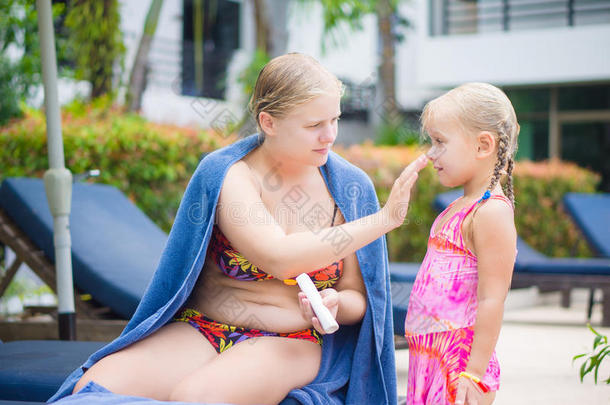 在热带海滩度假村的游<strong>泳池</strong>附近，母亲在女儿脸上涂<strong>防晒霜</strong>