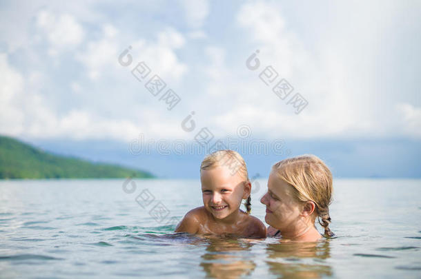年轻的母女俩在热带海洋的小岛上游泳玩得很开心。互相拥抱