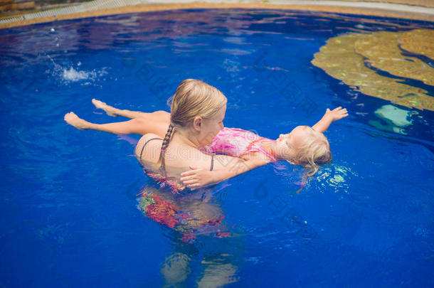 年轻的母亲和可爱的女儿在游<strong>泳池里玩耍</strong>。学习