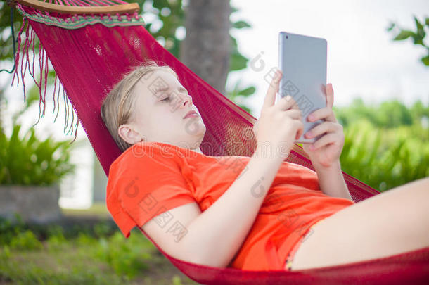 年轻女子在棕榈树下的吊床上放松地<strong>阅读</strong>电子平板<strong>阅读</strong>器