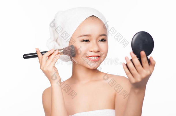 年轻的亚洲妇女用<strong>化妆</strong>刷在脸上涂粉。<strong>照镜子化妆</strong>。白底隔离