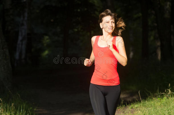 早晨在夏日公园里慢跑的快乐女孩。穿着运动服微笑的年轻白人妇女从for的阴影中跑出来