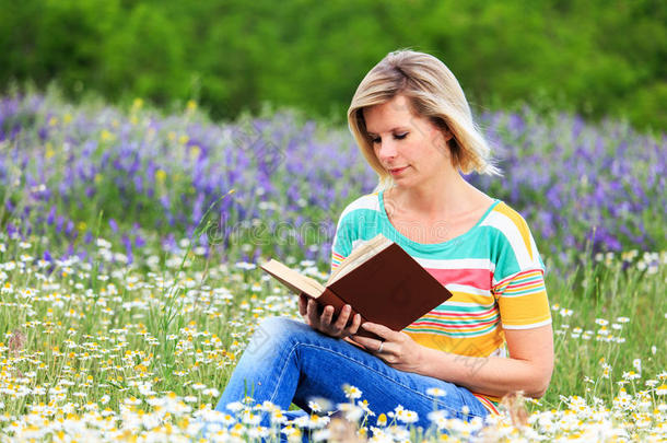金发女孩在花草丛生的草地上看书。
