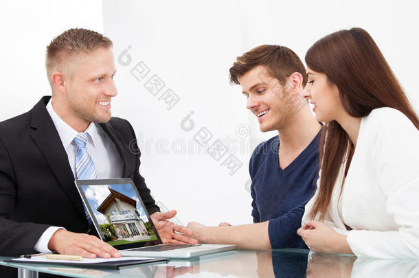 商人在笔记本电脑上给夫妇看房子的照片