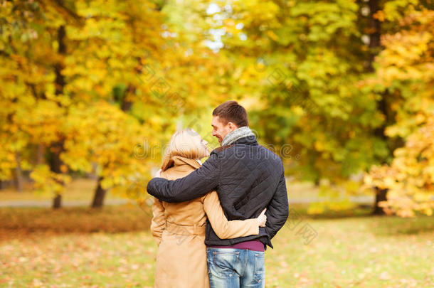 一对微笑的情侣从后面拥抱在秋天的公园里