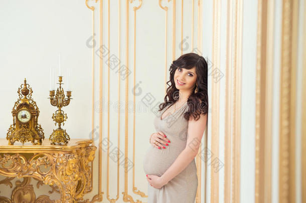 时尚的怀孕妈妈穿着金色的衣服拥抱肚子