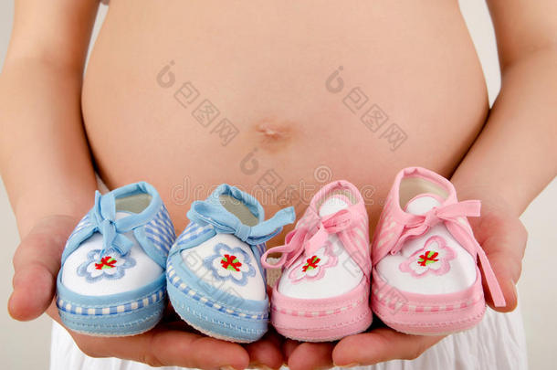 用粉色和蓝色的新生鞋来特写怀孕的肚子。。