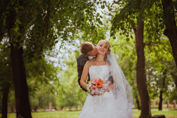 公园里的新郎新娘接吻。情侣新郎新娘在大自然的森林里举行婚礼，新郎新娘正在接吻