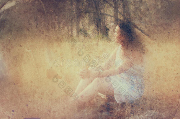 森林里坐在石头上的年轻女人的超现实的模糊背景。抽象而梦幻的概念。图像有质感和复古感