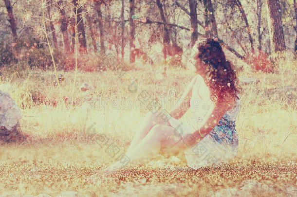 森林里坐在石头上的年轻女人的超现实的模糊背景。抽象而梦幻的概念。图像有质感和复古感