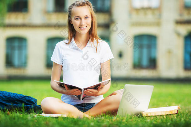 快乐漂亮的女学生坐在大学校园的草坪上，手里拿着<strong>笔记本电脑</strong>，用着<strong>笔记本电脑</strong>。