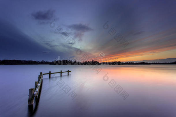 冬日的夕阳在宁静的湖面和木制的系泊柱上