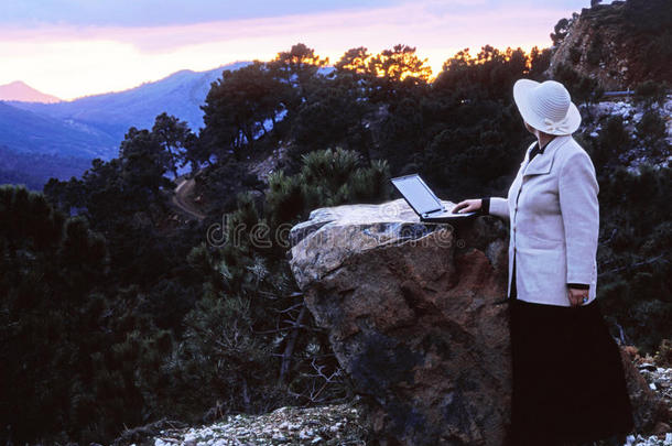 夕阳下，女人拿着笔记本站在山顶上