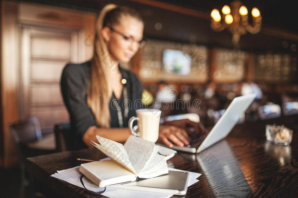 戴着眼镜的女商务人士在餐厅喝咖啡和笔记本电脑做笔记