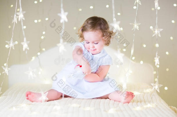 可爱的蹒跚学步的女孩玩她的玩具熊之间的软灯明星形状
