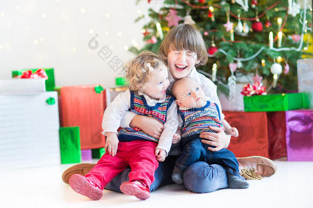 三个快乐的孩子——十几岁的男孩，蹒跚学步的女孩和他们刚出生的弟弟——在圣诞树下玩耍