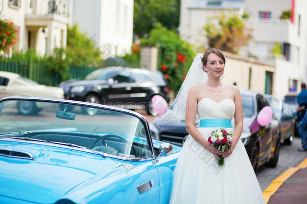 美丽的年轻新娘在蓝色汽车旁摆姿势