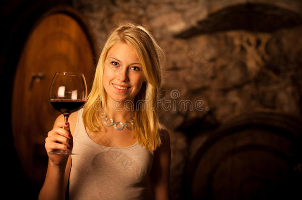 年轻漂亮的金发女子在酒窖里品尝红酒