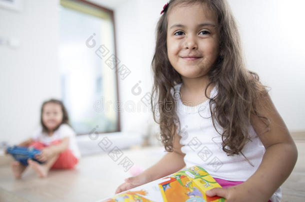 可爱女孩在家里拿着书和妹妹的画像