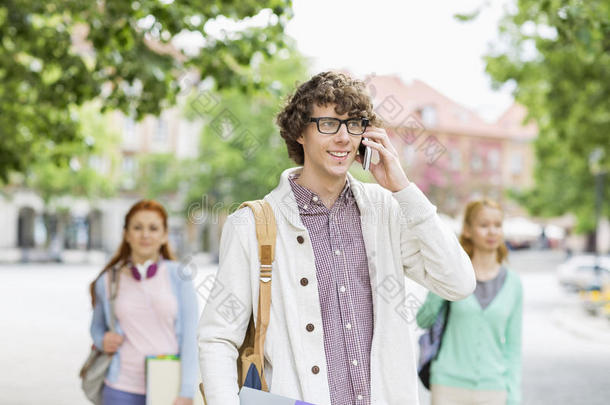 笑容可掬的年轻男学生在街上和朋友用手机聊天