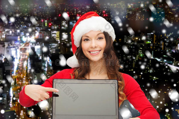微笑的女人戴着圣诞老人的帽子，手里拿着笔记本电脑