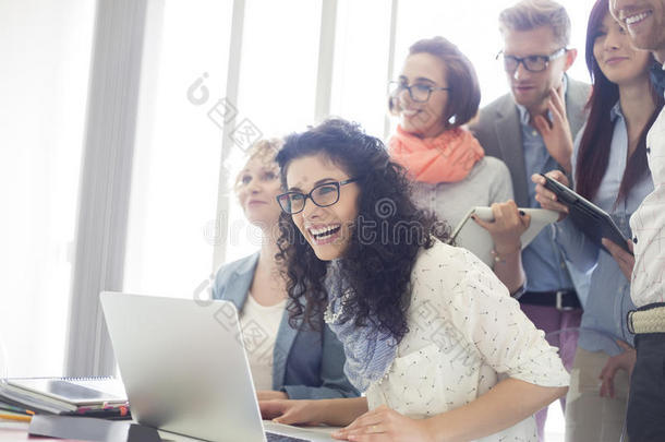 一群兴高采烈的商务人士在创意办公室的办公桌旁放着笔记本电脑