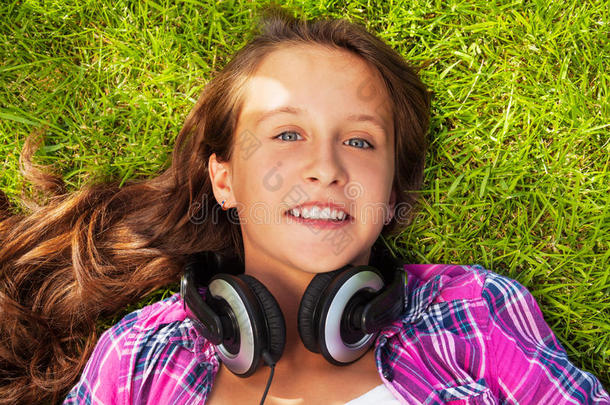 微笑的女孩<strong>戴</strong>着<strong>耳机</strong>躺在绿草地上