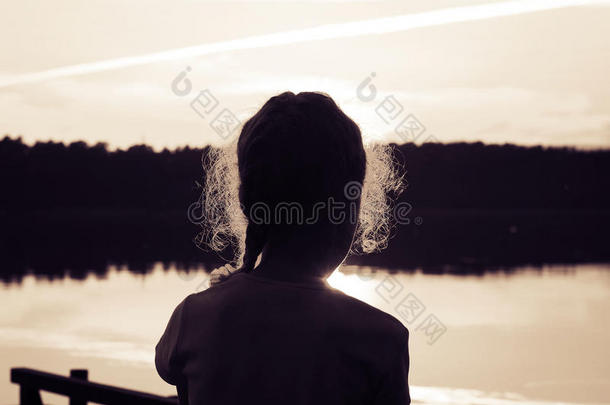 夕阳下湖面上可爱的小女孩的剪影。色调